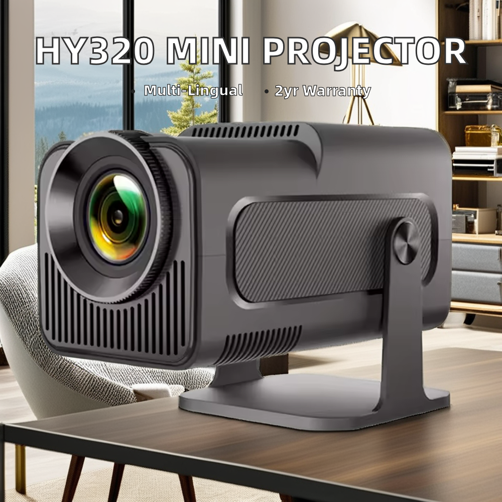 A compact black mini projector on a stand, shown on a wooden table in a modern living room setting. The text overlay at the top reads 'HY320 MINI PROJECTOR' with 'Multi-lingual' and '2yr Warranty' below it.