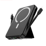 A black portable power bank with a built-in kickstand, shown with two black cables attached. The power bank features a white magnetic wireless charging symbol on its top surface and a digital battery percentage display on the front edge.