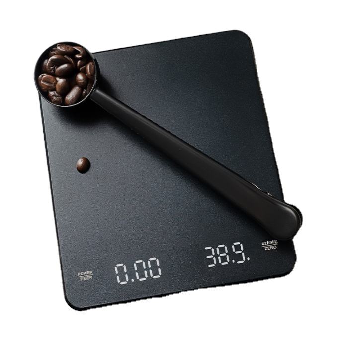 A black digital coffee scale with a matching scoop filled with coffee beans, shown on a plain white background.