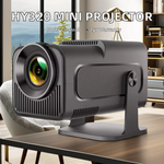 A compact black mini projector on a stand, shown on a wooden table in a modern living room setting. The text overlay at the top reads 'HY320 MINI PROJECTOR' with 'Multi-lingual' and '2yr Warranty' below it.
